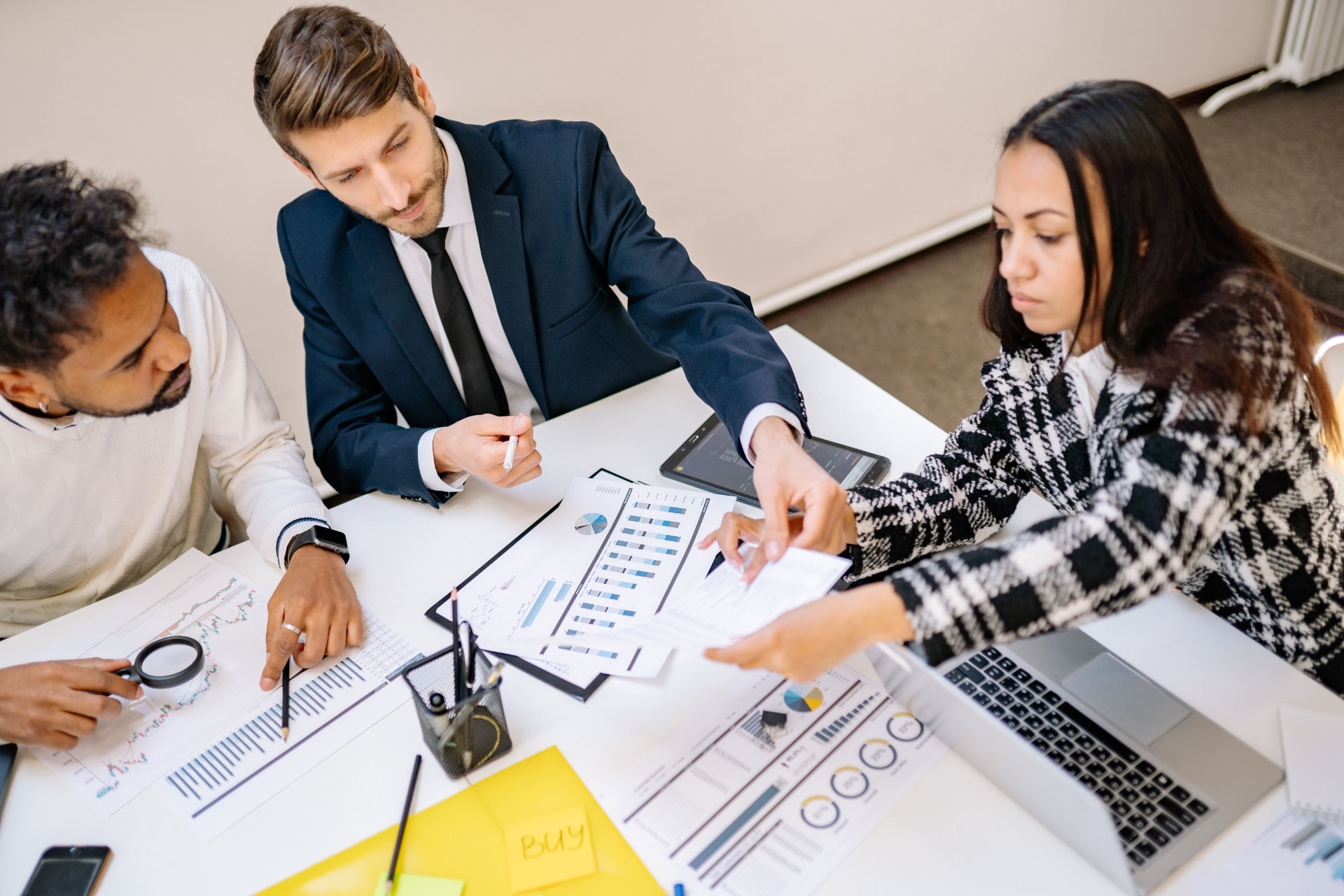 Three business professionals reviewing financial charts and documents together at a meeting table